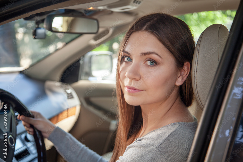 Young attractive caucasian woman with blue eyes and dark hair behind the wheel, driving a car. Happy smile, positive emotions, pretty sunny day. Outdoors, copy space.