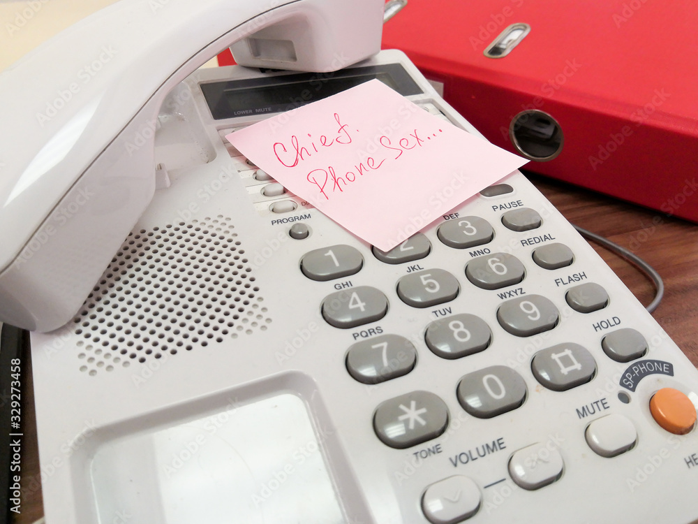 On the keyboard of the landline telephone lies a pink square leaflet with the inscription in red ink Chief, Phone sex On the keyboard of the landline telephone lies a pink square leaflet with the inscription in red ink Chief, Phone sex