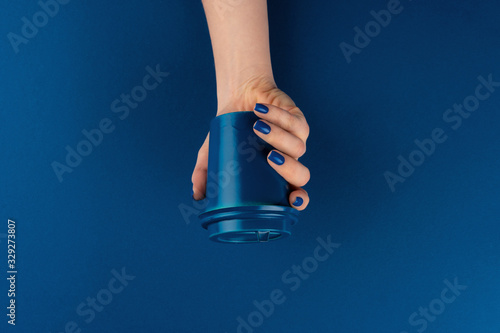 Female hand holding takeaway coffee cup gainst classic blue background, top view photo
