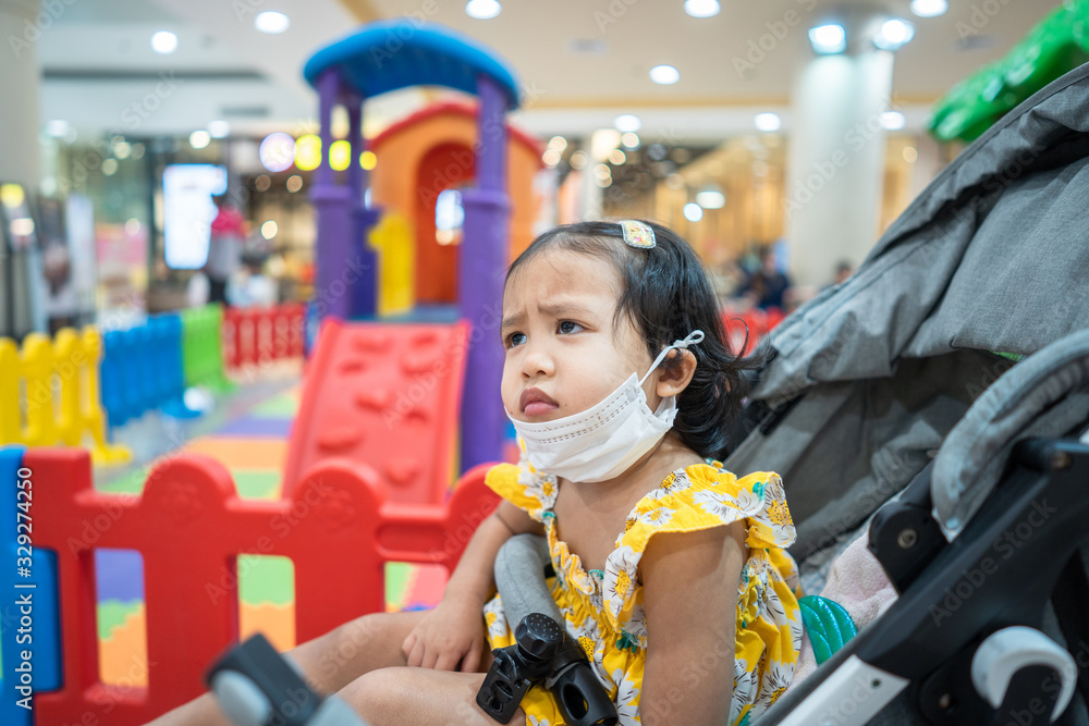 Little girl wearing medical face mask at playground in shopping mall to preventing flu, pollution and convid 19.