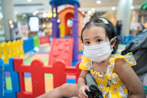 Little girl wearing medical face mask at playground in shopping mall to preventing flu, pollution and convid 19. photo