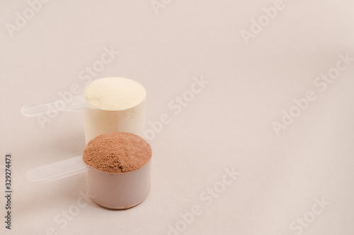 Whey protein powder in scoop and plastic shaker on neutral beige background