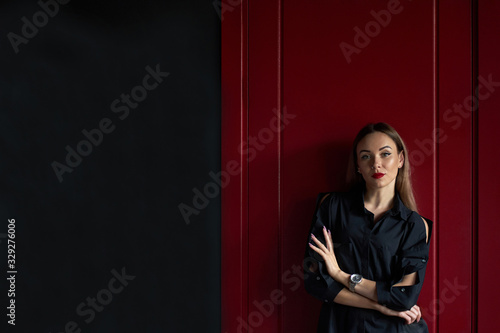 Portrait of young confident attractive stylish womanl with long hair and red painted lips wearing fashionable black blouse. Studio shot on red and grey wall background. photo