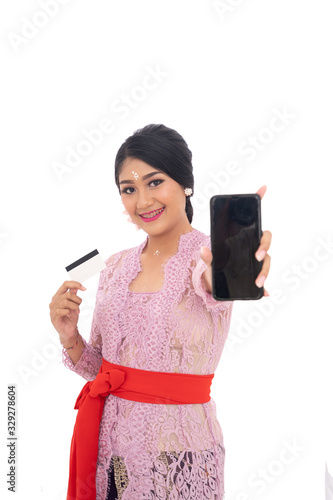 smiling woman wearing Balinese traditional clothes hold credit card clothes with shows her phone to camera