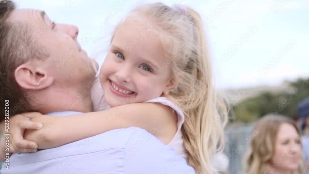 Middle-aged father embraces his daughter. Fair-haired little girl smiles happily Middle-aged father embraces his daughter. Fair-haired little girl smiles happily