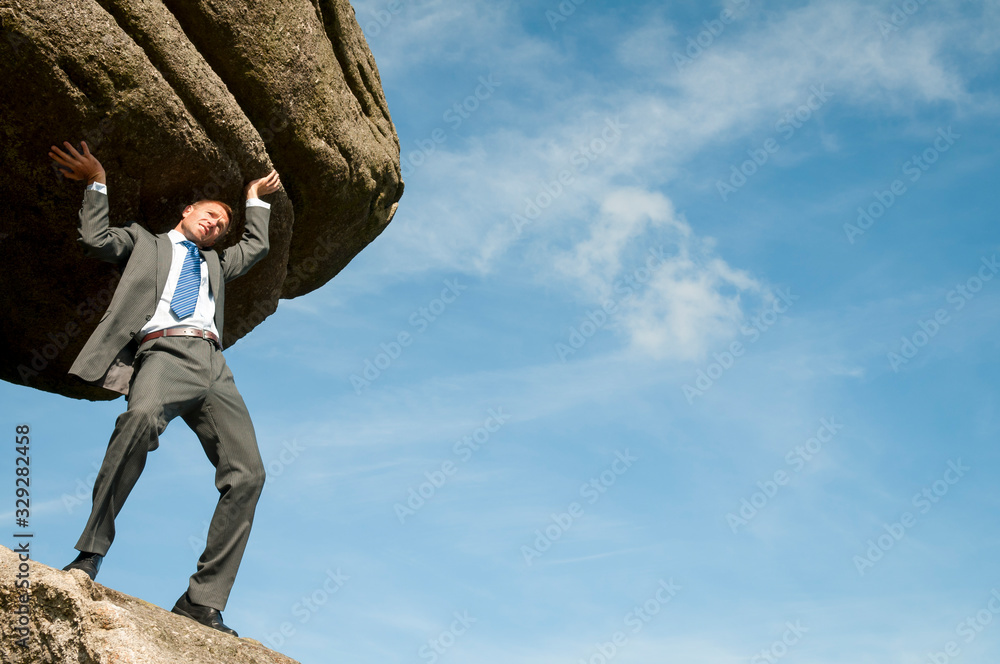 Strong businessman struggling to lift massive boulder into blue sky copy space Strong businessman struggling to lift massive boulder into blue sky copy space