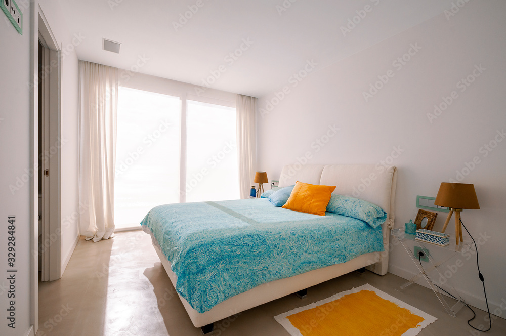 Modern bedroom in green overlooking the sea. Blue and yellow pillows, carpet and blanket.