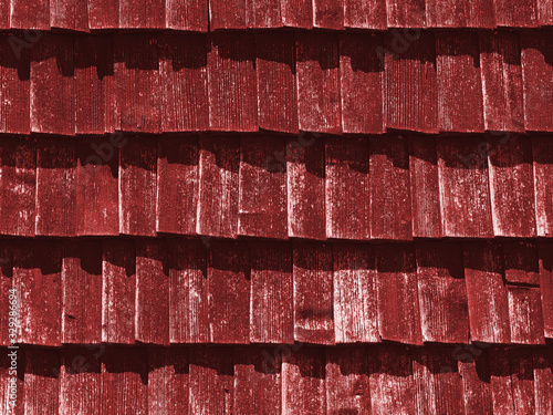 Red texture of wooden tile roof. Shingle aged wooden Background. Backdrop with small overlapping colored wooden shingles on roof