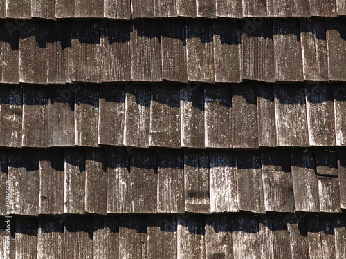 Brown texture of wooden tile roof. Shingle aged wooden Background. Backdrop with small overlapping colored wooden shingles on roof