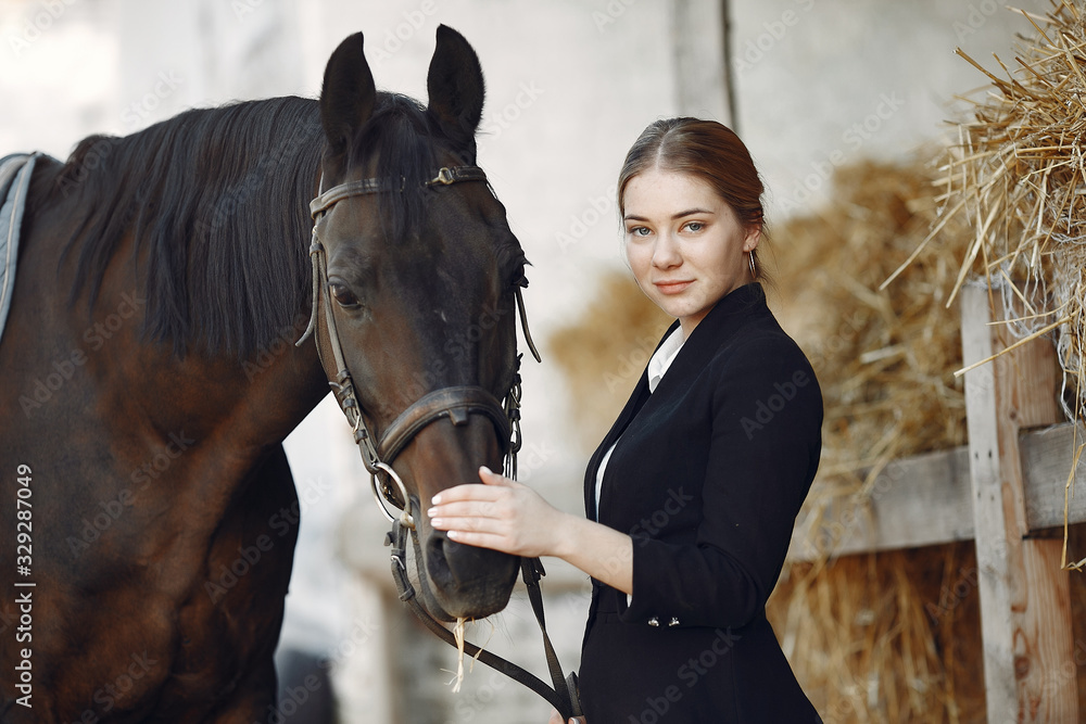 Obraz premium Woman standing near horse. Rider in a black uniform. Girl feeds horse hay