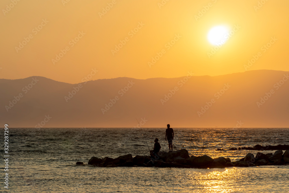 Silhouettes Of Men Fishing On Rocks At Sunset Silhouettes Of Men Fishing On Rocks At Sunset