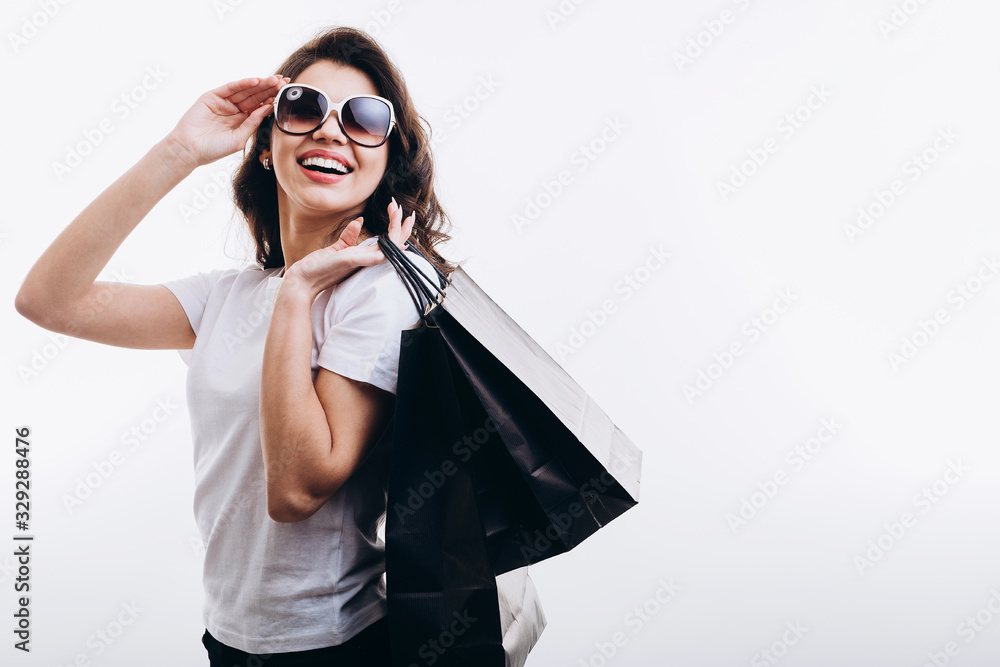 Happy cute female customer with black paper bags adjusting sunglasses isolated white background copyspace Happy cute female customer with black paper bags adjusting sunglasses isolated white background copyspace