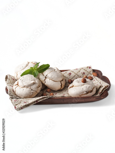 food photography of textured beige homemade meringue with mint and nuts on a rustic wooden dish on a white background isolated