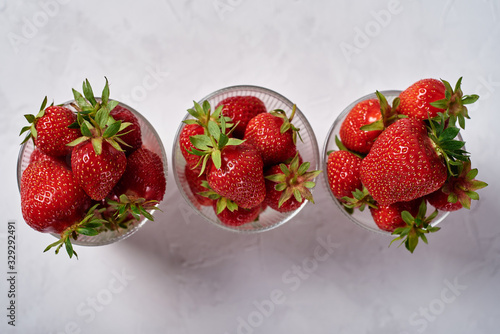 Red ripe strawberries in glass bowls on gray table background, copy space. Healthy food concept
