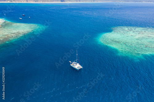 Aerial view of a sailboat next to a large, offshore tropical coral reef