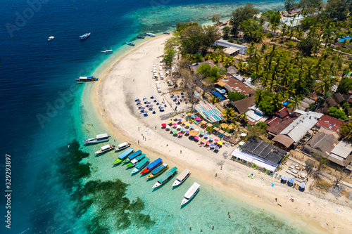Top down aerial view of colorful boats and sunshades on a tropical beach on a small island fringed by a coral reef