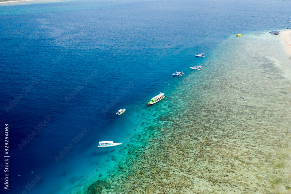 Aerial drone view of boats, swimmers and snorkelers above a beautiful tropical coral reef on Gili Air, Indonesia