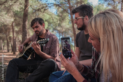 Friends in the field singing and playing a guitar and recording with the mobile phone