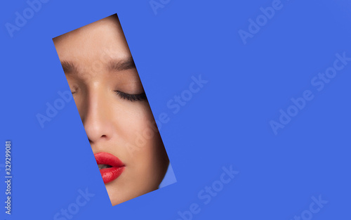 Beautiful woman with red lips peeping out torn paper © Prostock-studio