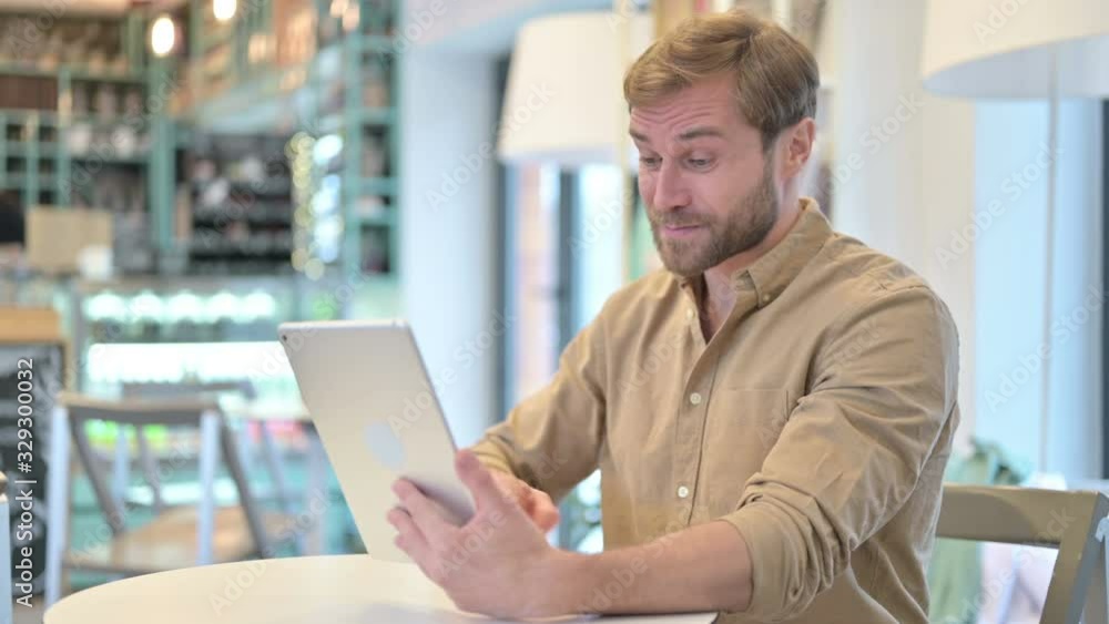 Handsome Man Celebrating Success on Tablet in Cafe Handsome Man Celebrating Success on Tablet in Cafe