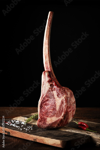 Raw Tomahawk steak on a beef bone dry aged on a dark background photo