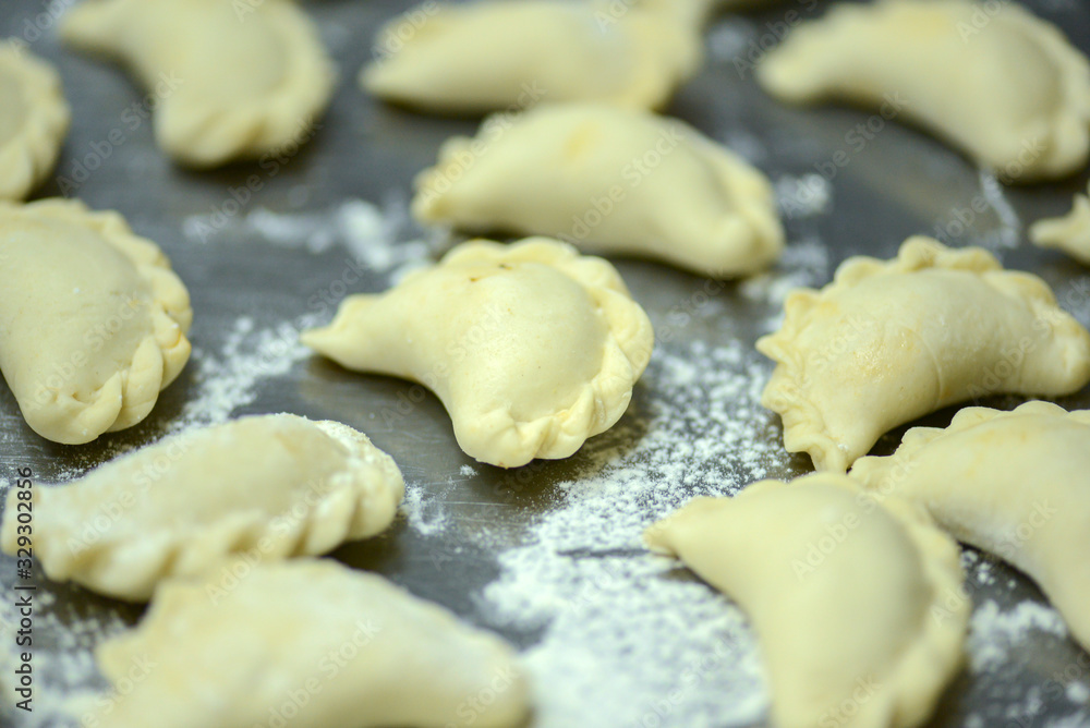 Uncooked russian vareniki on metal tray with flour. Process of making vareniki. Uncooked russian vareniki on metal tray with flour. Process of making vareniki.