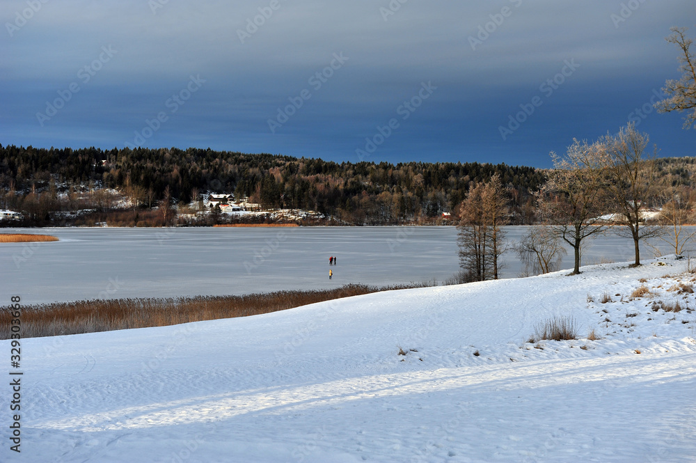 Beautiful winter scene of Borrevannet lake in Horten, Norway. Ski track in the front of image.  People skating on the lake in the background. Pretty weather on a frosty day.