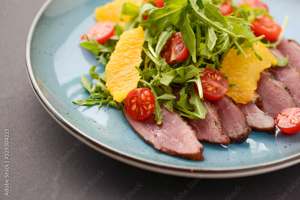 Italian ham prosciutto salad with orange, cherry tomatoes and arugula served on a blue plate on dark background