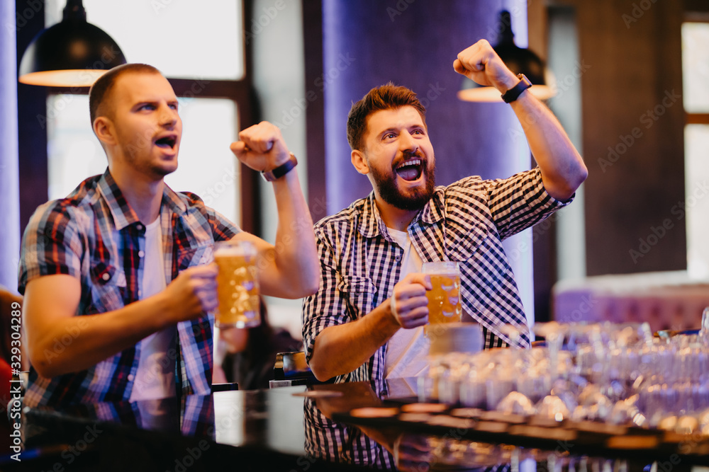 Happy two men shouting while watching football match broadcast in pub