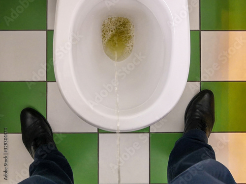 Foto Top view of male feet and a toilet bowl into which a stream of urine flows