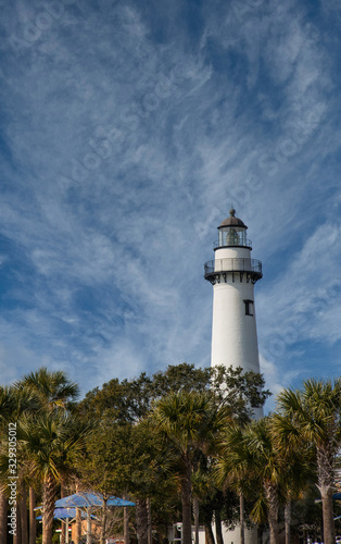 A white brick lighthouse under clear blue skies beyond a green park