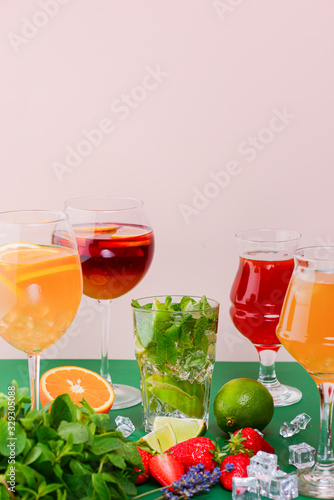 Five tropical mixed drinks, orange, lemon and raspberries cocktails over bright pastel green background.