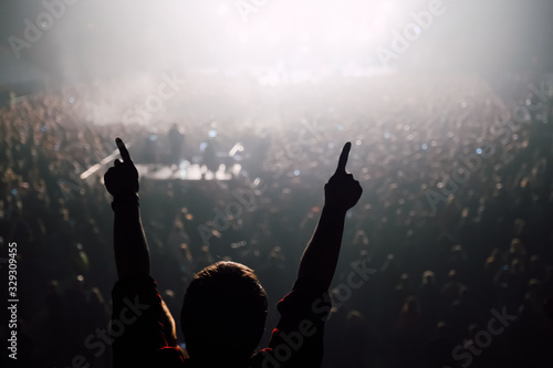 Man with hands raised up at the stadium concert with stage lights and crowd at background