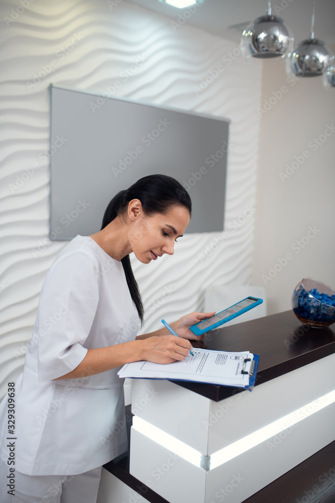 Dark-haired receptionist holding tablet and making notes