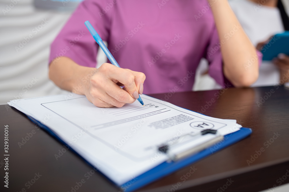 Receptionist wearing purple uniform holding pen while making notes Receptionist wearing purple uniform holding pen while making notes