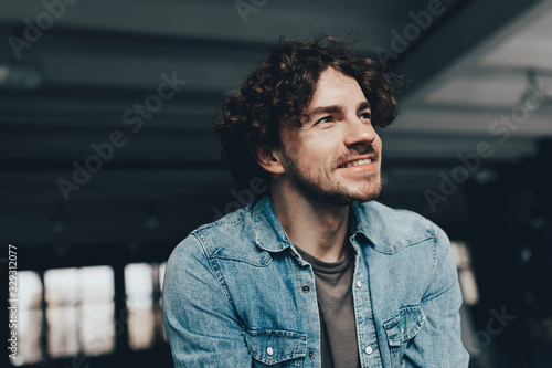 Young and confident. Handsome young man with curly hair in light blue jeans shirt looking in away