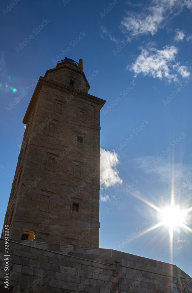 couple watching the hercules tower with the sun placed to the right of the monument