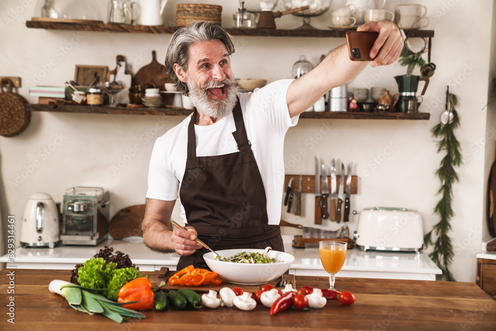 Image of excited gray-haired man taking selfie and preparing salad