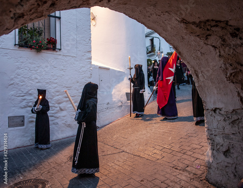 Fotografía Nazarenos con velas y un estandarte rojo al inicio de una procesión nocturna de