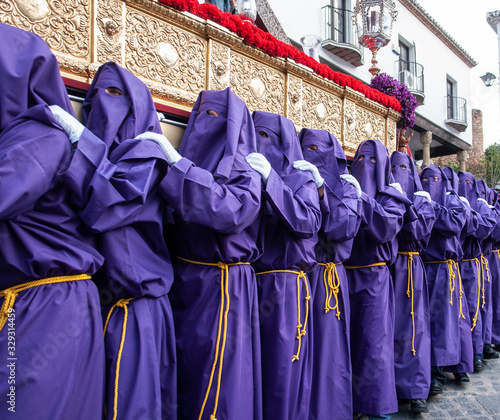 Nazarenos portando un trono de Semana Santa con túnica y capirote de color violeta photo
