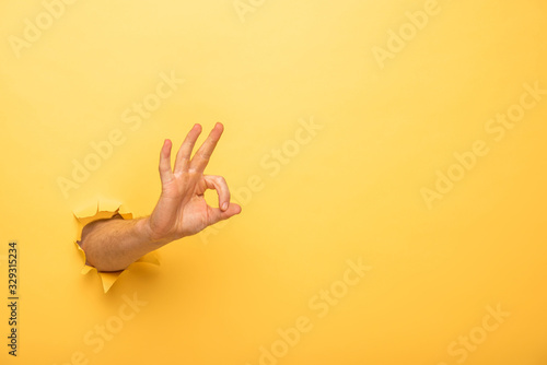 cropped view of man showing ok sign through yellow paper hole photo