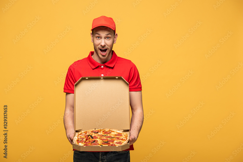 shocked delivery man in red uniform showing box with delicious pizza isolated on yellow shocked delivery man in red uniform showing box with delicious pizza isolated on yellow