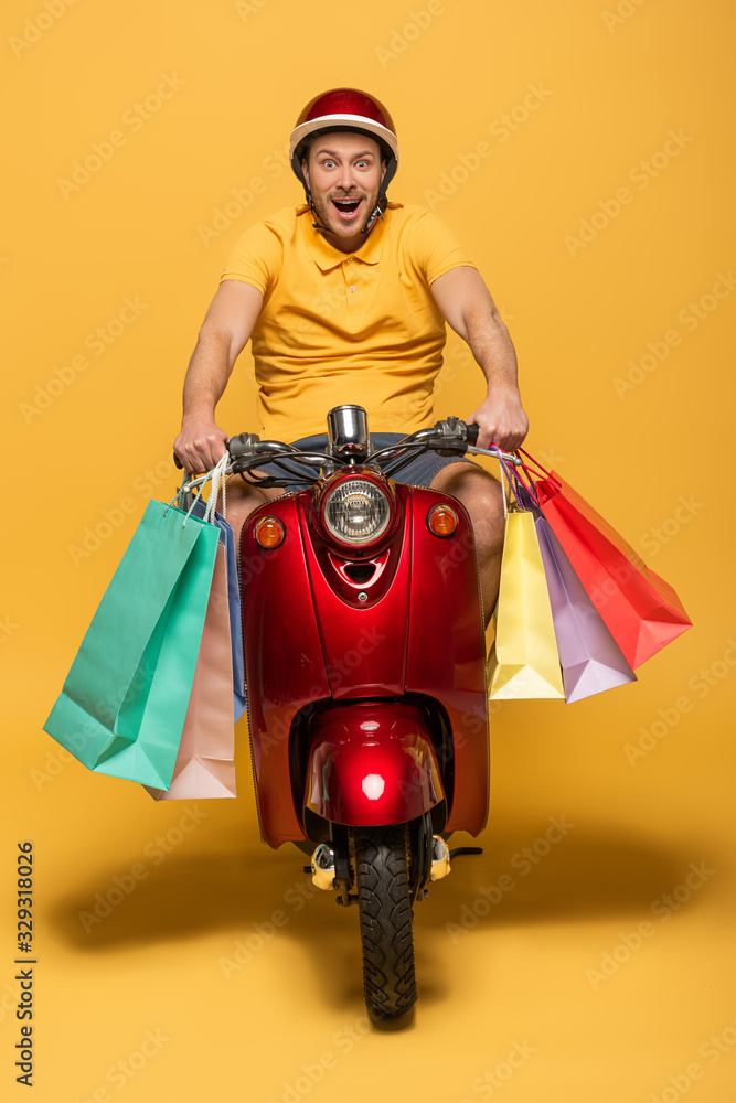 happy delivery man in yellow uniform riding scooter with shopping bags on yellow background happy delivery man in yellow uniform riding scooter with shopping bags on yellow background
