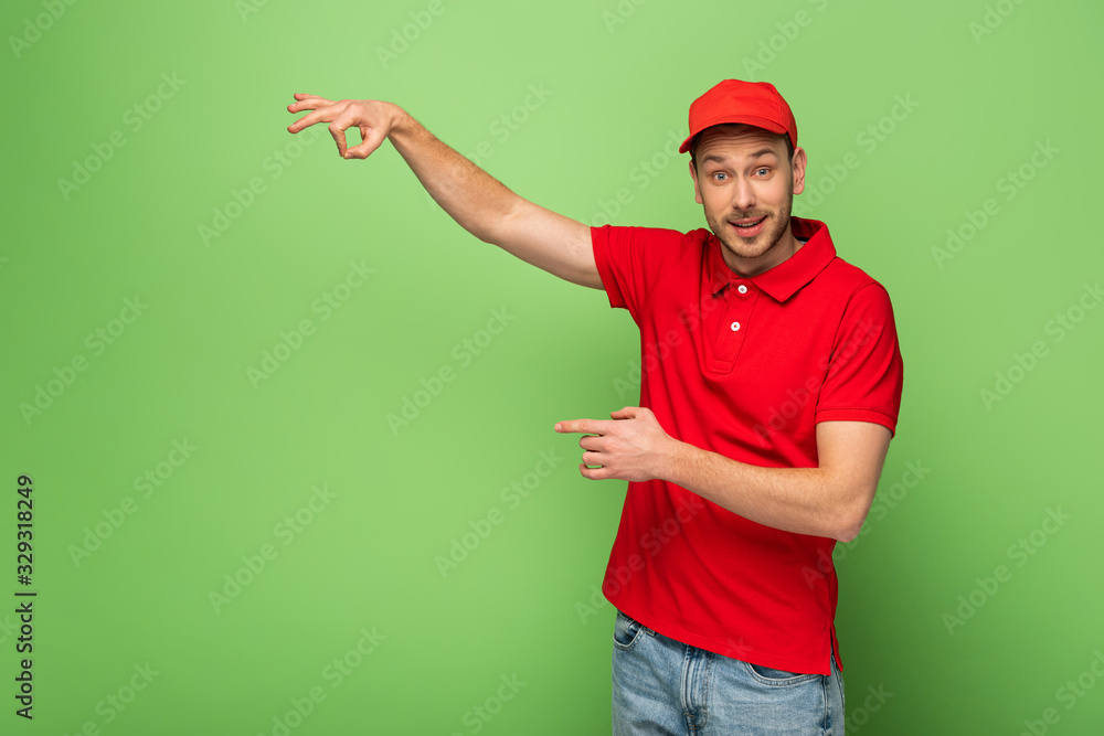 delivery man in red uniform pointing with finger aside on green background delivery man in red uniform pointing with finger aside on green background