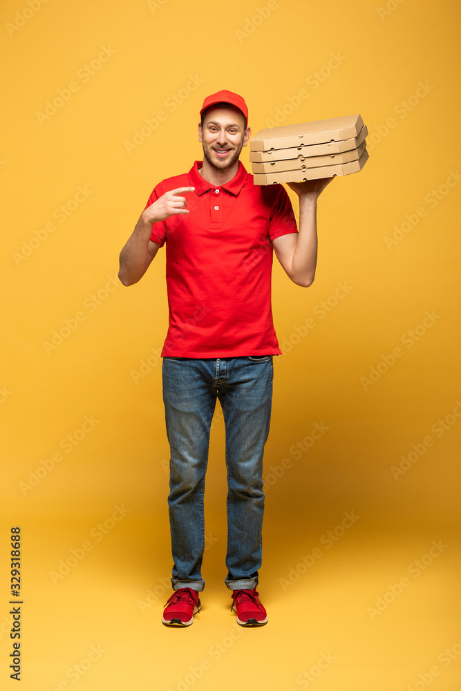 happy delivery man in red uniform pointing with finger at pizza boxes on yellow happy delivery man in red uniform pointing with finger at pizza boxes on yellow