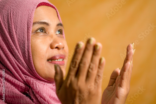 isolated studio portrait of happy and positive senior muslim woman in her 50s wearing traditional Islam hijab head scarf praying in Islamic culture and religion concept