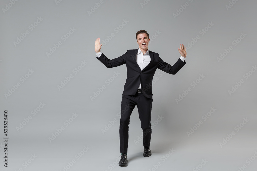 Cheerful laughing young business man in classic black suit shirt posing isolated on grey background studio portrait. Achievement career wealth business concept. Mock up copy space. Spreading hands. Cheerful laughing young business man in classic black suit shirt posing isolated on grey background studio portrait. Achievement career wealth business concept. Mock up copy space. Spreading hands.