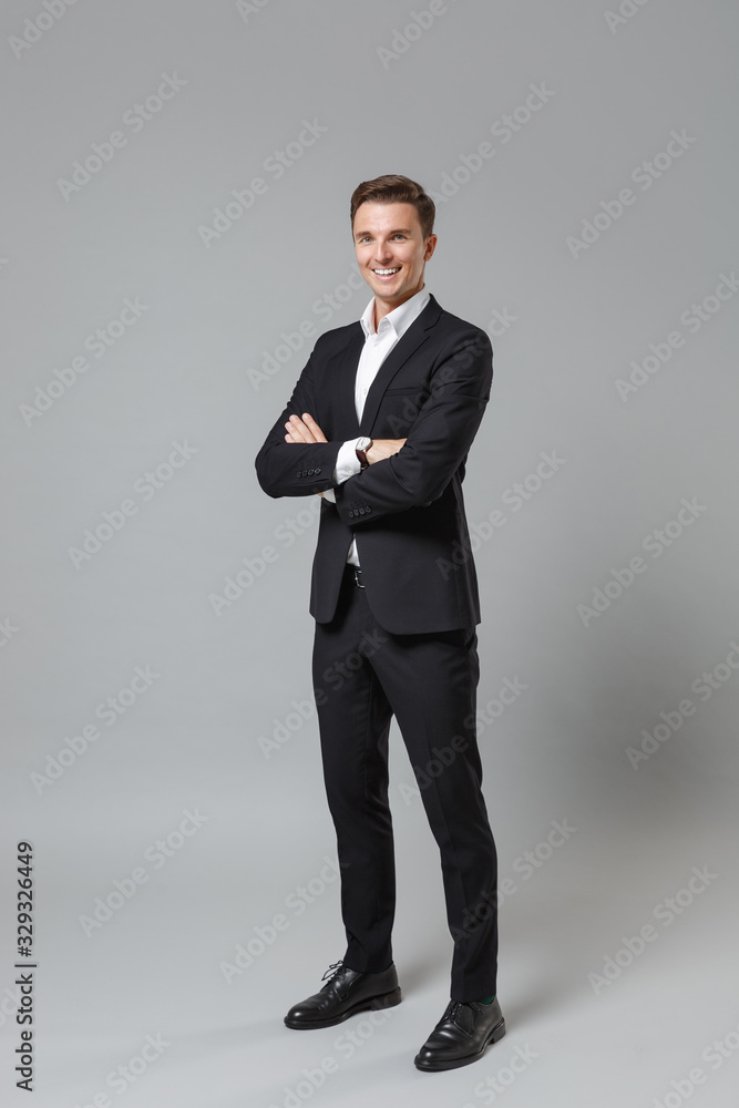 Successful young business man in classic black suit shirt posing isolated on grey wall background studio portrait. Achievement career wealth business concept. Mock up copy space. Hold hands crossed. Successful young business man in classic black suit shirt posing isolated on grey wall background studio portrait. Achievement career wealth business concept. Mock up copy space. Hold hands crossed.