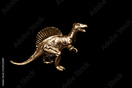 Golden toy dinosaur isolated on black background.