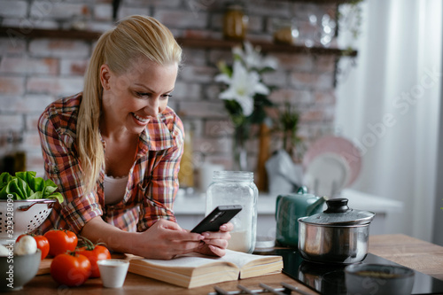 Beautiful woman in kitchen. Young woman writing message on phone.  © JustLife